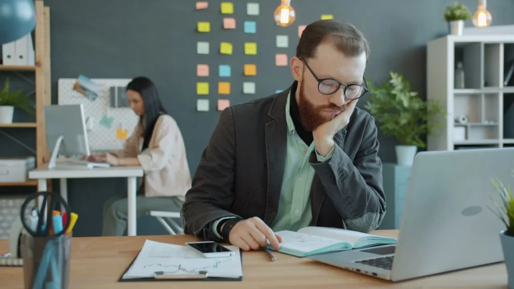 Erschöpfter Mann sitzt vor einem Laptop an einem Schreibtisch