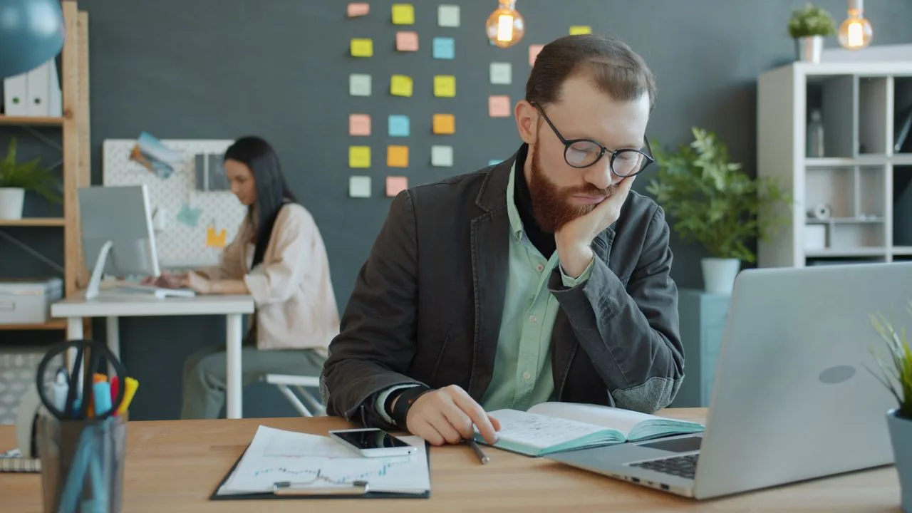 Erschöpfter Mann sitzt vor einem Laptop an einem Schreibtisch