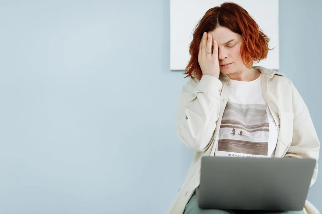 Verunsicherte Frau sitzt mit der Hand am Gesicht vor einem Laptop