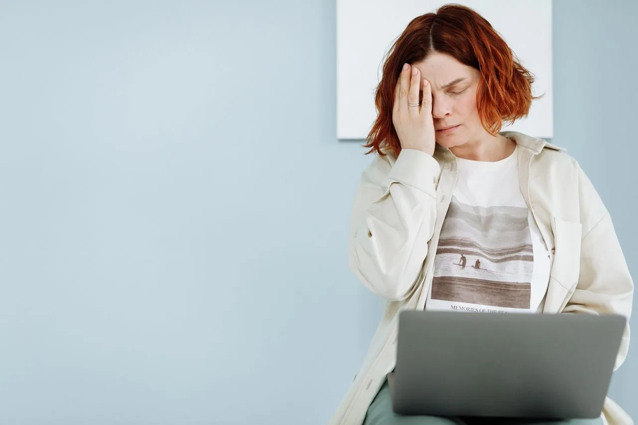 Verunsicherte Frau sitzt mit der Hand am Gesicht vor einem Laptop