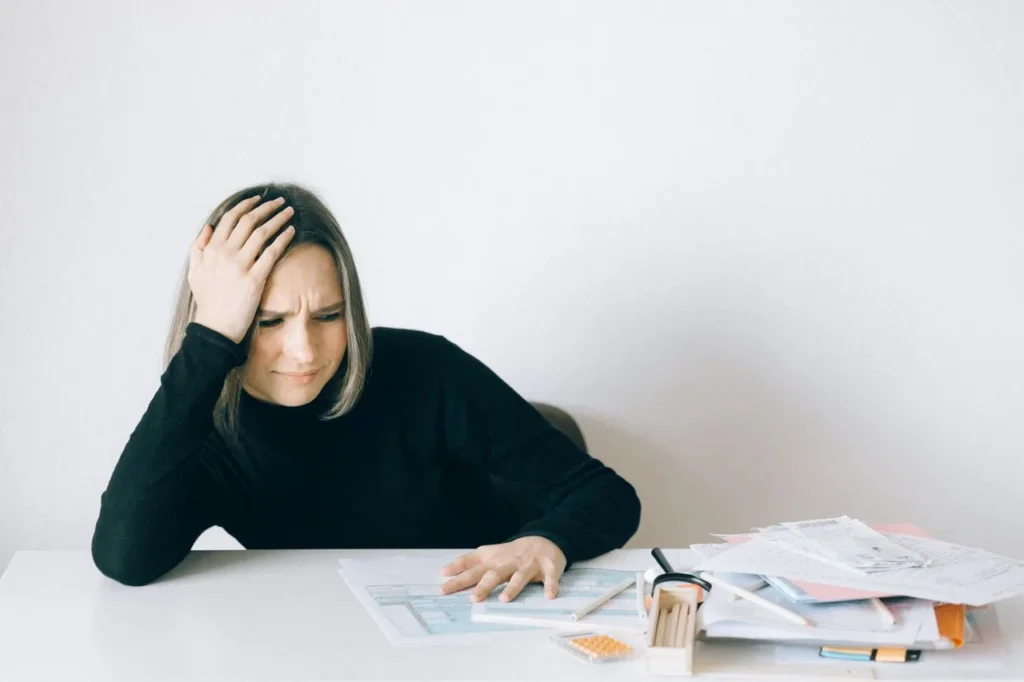 A tense woman sits at a desk surrounded by papers