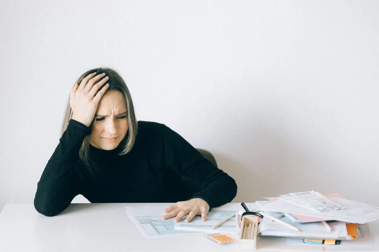 A tense woman sits at a desk surrounded by papers